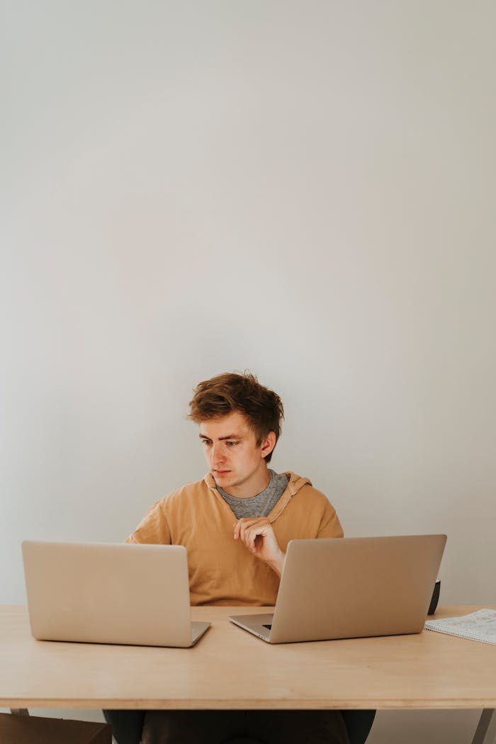 Mastering the First Impression: Your intriguing post title goes here Focused young adult engaged in programming using two laptops at a desk.